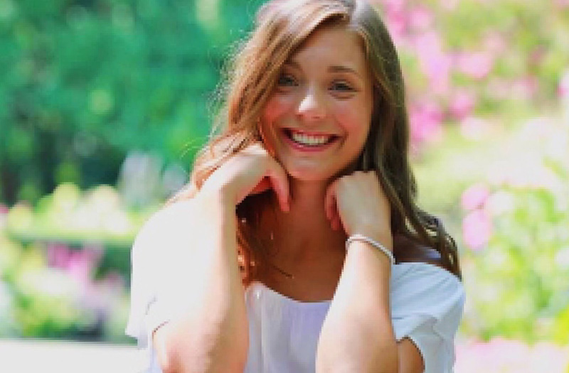 A smiling woman poses in front of a flower garden.